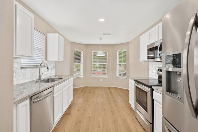 kitchen with appliances with stainless steel finishes, pendant lighting, white cabinetry, sink, and light wood-type flooring