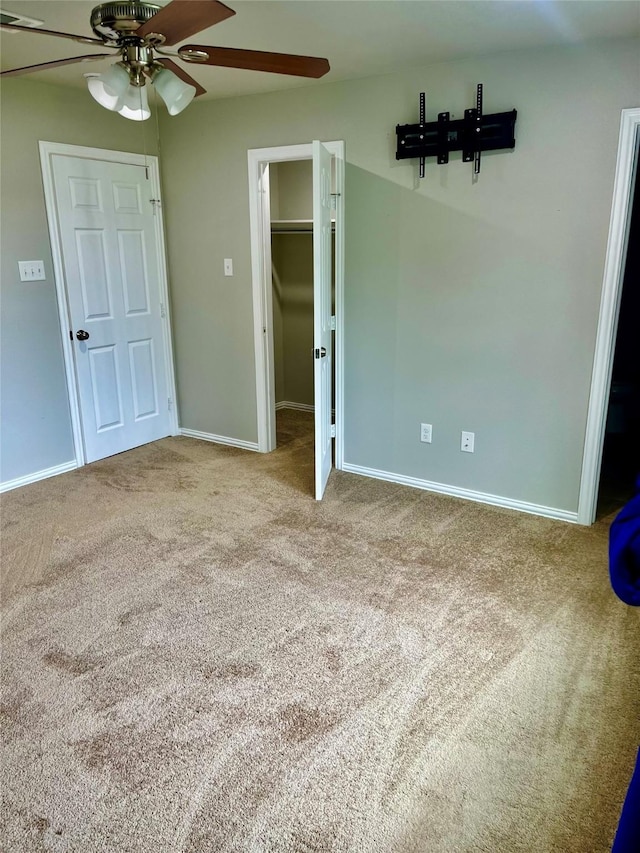 unfurnished bedroom featuring a walk in closet, light colored carpet, a closet, and ceiling fan