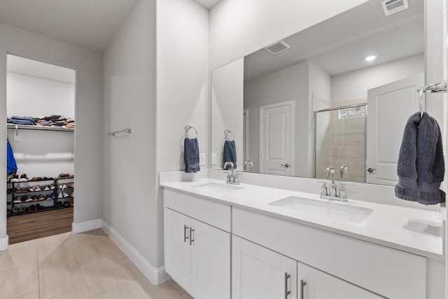 full bath featuring a stall shower, a spacious closet, visible vents, and a sink