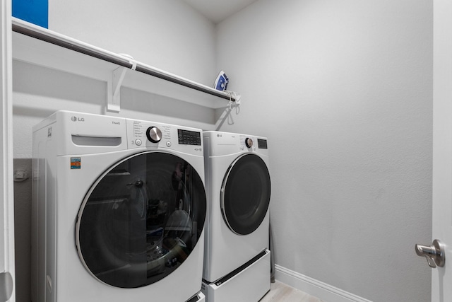 laundry room featuring laundry area, light wood-style flooring, washing machine and dryer, and baseboards