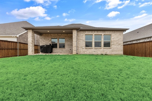 back of property with a patio, brick siding, a fenced backyard, and a lawn