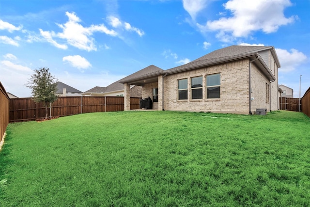 rear view of house with a yard, a fenced backyard, and brick siding