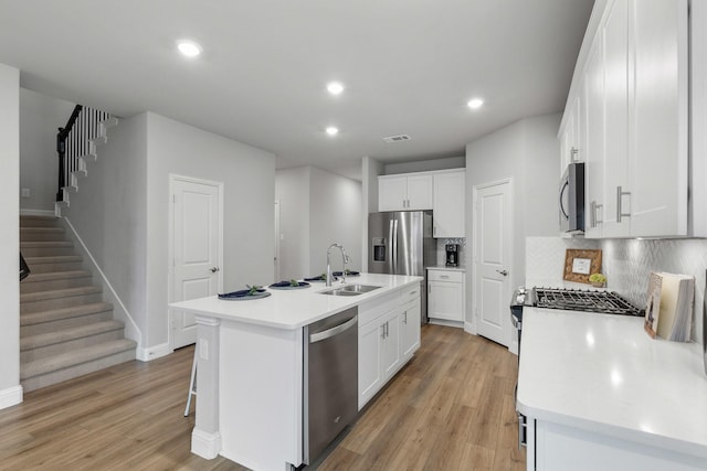 kitchen featuring appliances with stainless steel finishes, sink, white cabinets, a center island with sink, and light hardwood / wood-style flooring