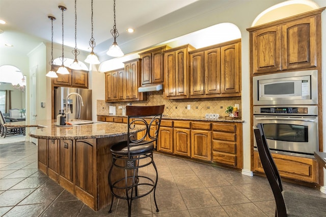 kitchen featuring sink, a breakfast bar area, pendant lighting, stainless steel appliances, and a kitchen island with sink