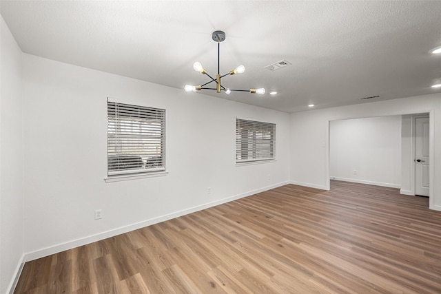 empty room featuring hardwood / wood-style floors, a notable chandelier, and a textured ceiling