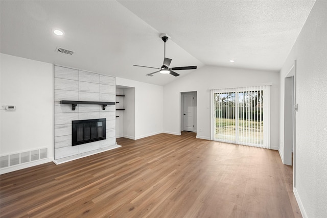 unfurnished living room featuring vaulted ceiling, a textured ceiling, light wood-type flooring, a tile fireplace, and ceiling fan