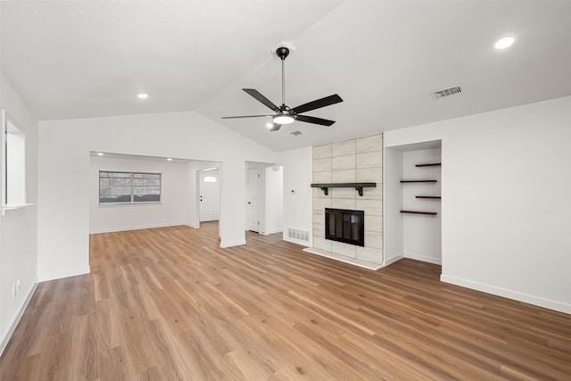 unfurnished living room with ceiling fan, vaulted ceiling, a tile fireplace, and light hardwood / wood-style flooring