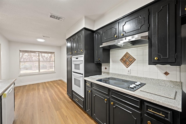 kitchen featuring backsplash, white appliances, a textured ceiling, and light wood-type flooring