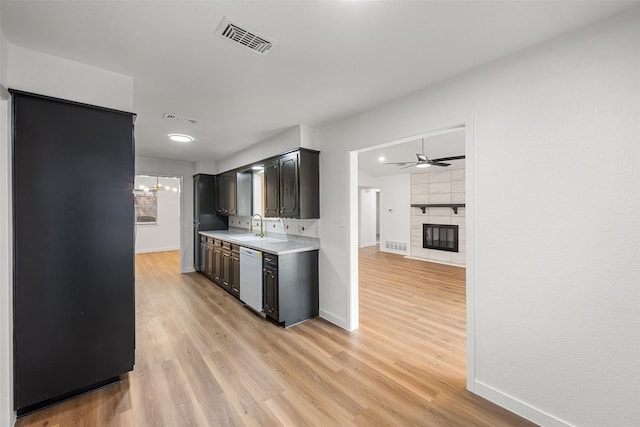 kitchen featuring sink, a tile fireplace, dishwasher, ceiling fan with notable chandelier, and light wood-type flooring