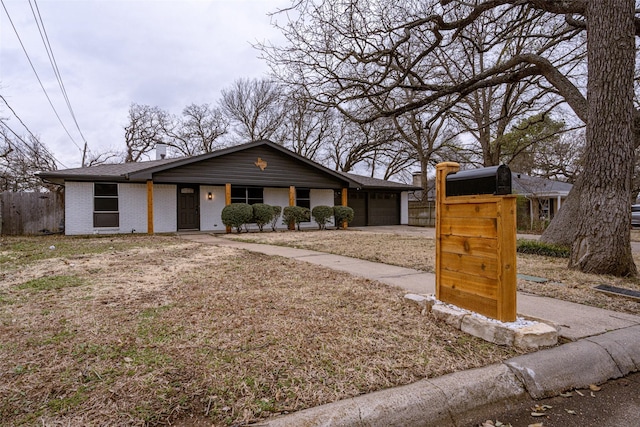 view of front of house featuring an attached garage, fence, brick siding, and driveway