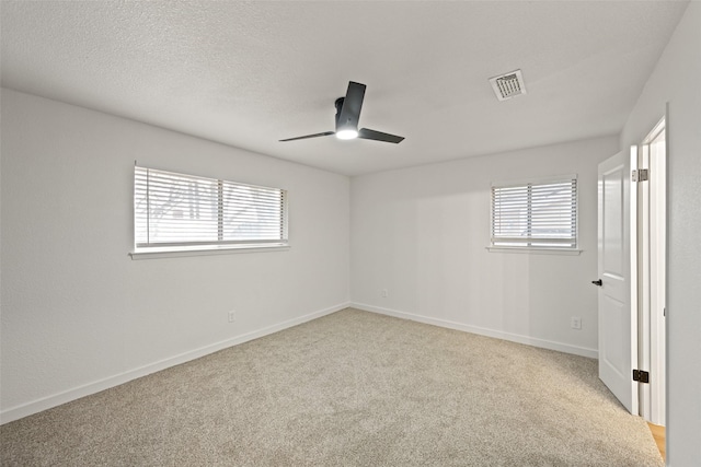 empty room featuring ceiling fan, plenty of natural light, light colored carpet, and a textured ceiling