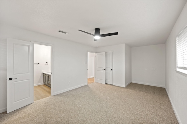 unfurnished bedroom with ensuite bathroom, light carpet, and ceiling fan