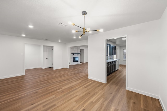 unfurnished living room with an inviting chandelier, sink, a fireplace, and hardwood / wood-style floors