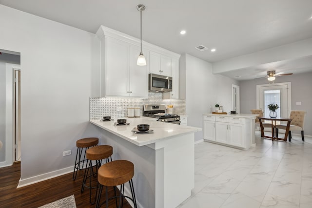 kitchen featuring a breakfast bar, appliances with stainless steel finishes, white cabinetry, hanging light fixtures, and kitchen peninsula