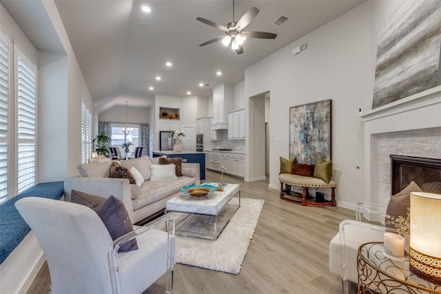 living room with high vaulted ceiling, ceiling fan with notable chandelier, a fireplace, and light wood-type flooring