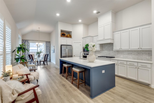 kitchen featuring appliances with stainless steel finishes, decorative light fixtures, white cabinetry, an island with sink, and a breakfast bar area