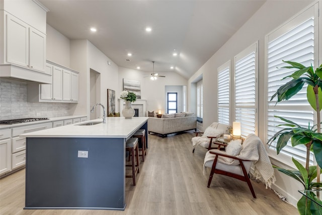 kitchen with sink, a breakfast bar area, a kitchen island with sink, white cabinetry, and stainless steel gas stovetop