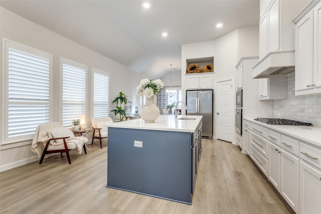 kitchen featuring sink, tasteful backsplash, light wood-type flooring, appliances with stainless steel finishes, and a kitchen island with sink