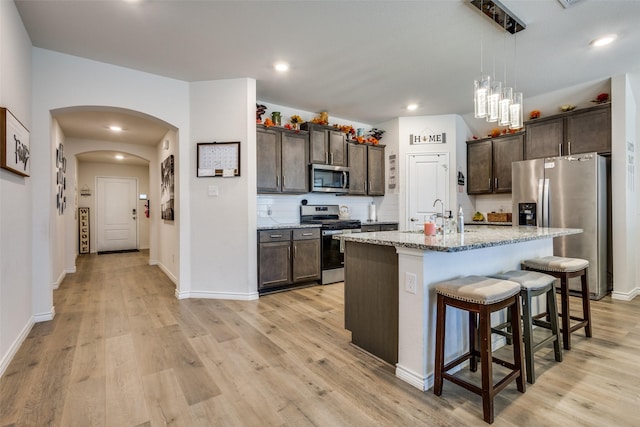 kitchen featuring arched walkways, dark brown cabinets, appliances with stainless steel finishes, tasteful backsplash, and a kitchen bar