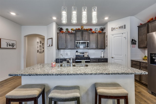 kitchen with arched walkways, a breakfast bar area, wood finished floors, stainless steel appliances, and a sink