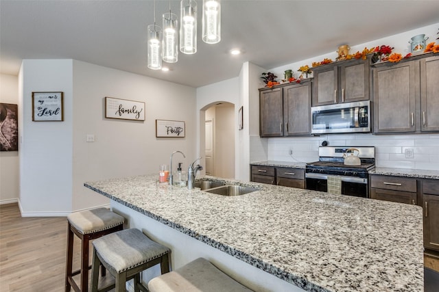 kitchen with stainless steel appliances, backsplash, a sink, and light stone countertops