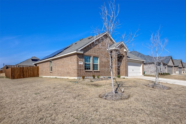 view of front of property with driveway, solar panels, an attached garage, fence, and brick siding