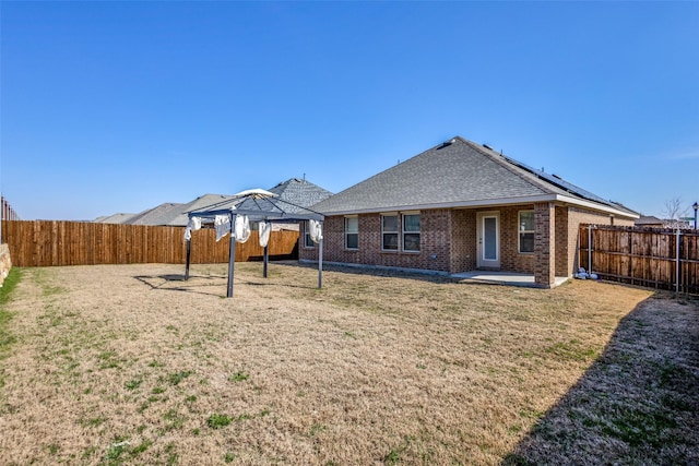 rear view of property with a yard, a gazebo, brick siding, and a fenced backyard