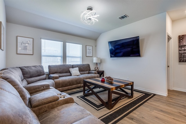 living area featuring lofted ceiling, visible vents, baseboards, light wood finished floors, and an inviting chandelier