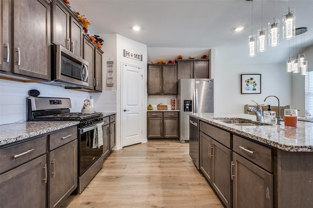 kitchen featuring light stone counters, stainless steel appliances, a sink, dark brown cabinetry, and light wood-type flooring