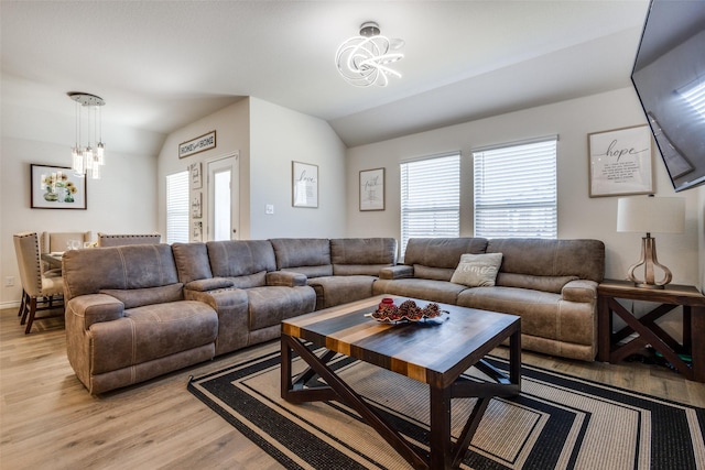 living room featuring a wealth of natural light, vaulted ceiling, a notable chandelier, and light wood finished floors