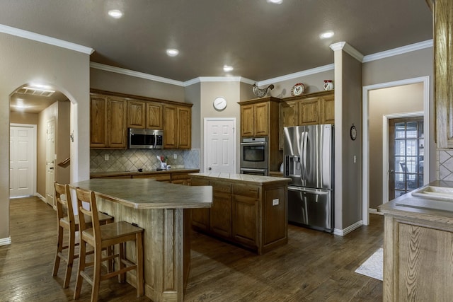 kitchen featuring dark wood-type flooring, a center island, ornamental molding, appliances with stainless steel finishes, and decorative backsplash