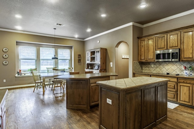 kitchen with tasteful backsplash, hanging light fixtures, dark hardwood / wood-style floors, a kitchen island, and black electric stovetop