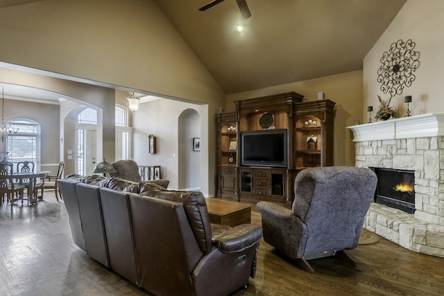 living room with crown molding, hardwood / wood-style flooring, ceiling fan, high vaulted ceiling, and a stone fireplace