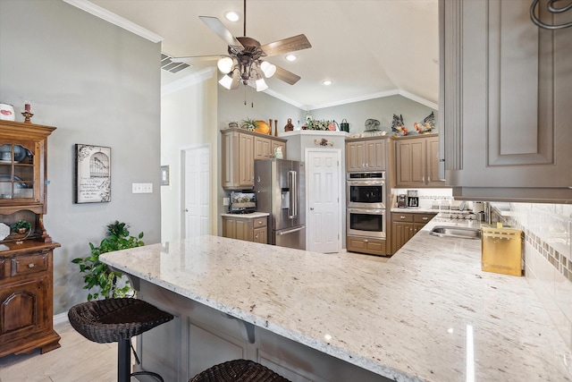 kitchen with vaulted ceiling, appliances with stainless steel finishes, a breakfast bar area, ornamental molding, and kitchen peninsula