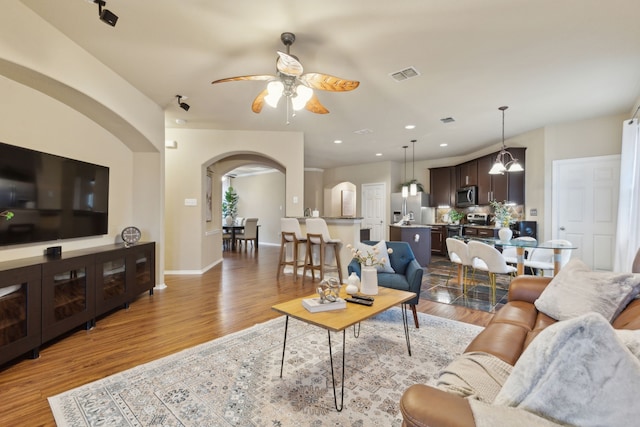 living area featuring baseboards, arched walkways, wood finished floors, and ceiling fan with notable chandelier