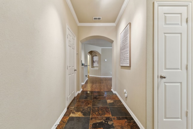 corridor featuring arched walkways, stone tile flooring, visible vents, ornamental molding, and baseboards