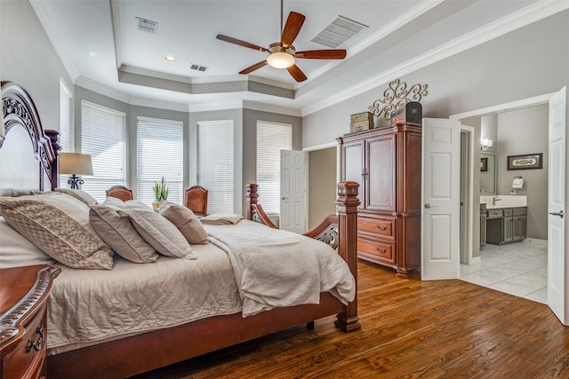 bedroom with ensuite bath, ornamental molding, ceiling fan, a raised ceiling, and light wood-type flooring