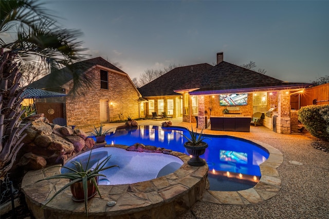 pool at dusk featuring an in ground hot tub, an outdoor kitchen, an outdoor living space, and a patio area