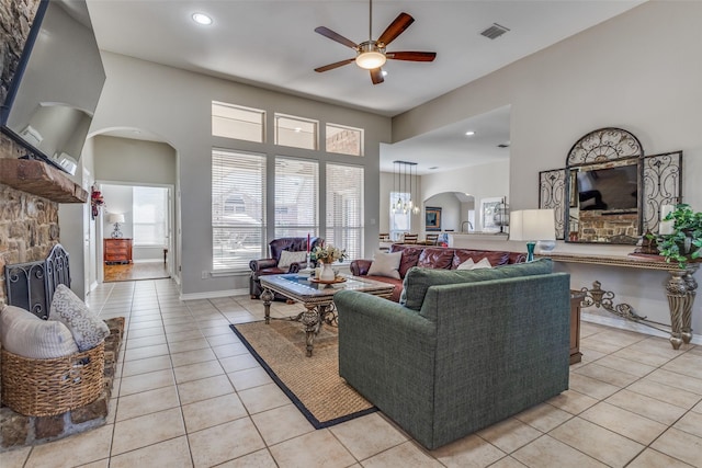 living room featuring light tile patterned floors, a stone fireplace, ceiling fan, and a high ceiling