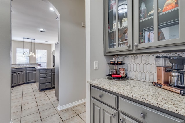 kitchen with gray cabinets, decorative light fixtures, decorative backsplash, light tile patterned floors, and light stone counters