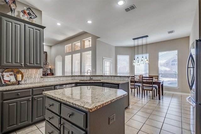 kitchen with appliances with stainless steel finishes, decorative light fixtures, sink, a center island, and light stone counters