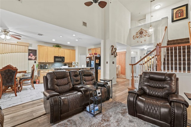 living room featuring a towering ceiling, ceiling fan, and light wood-type flooring