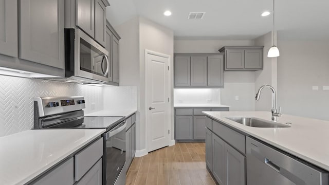 kitchen with sink, gray cabinets, hanging light fixtures, stainless steel appliances, and light wood-type flooring