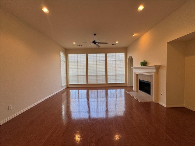 unfurnished living room featuring dark wood-type flooring, a wealth of natural light, a tile fireplace, and ceiling fan