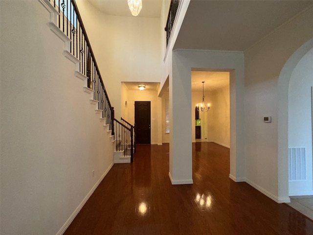 interior space featuring dark hardwood / wood-style flooring, a notable chandelier, a towering ceiling, and ornamental molding