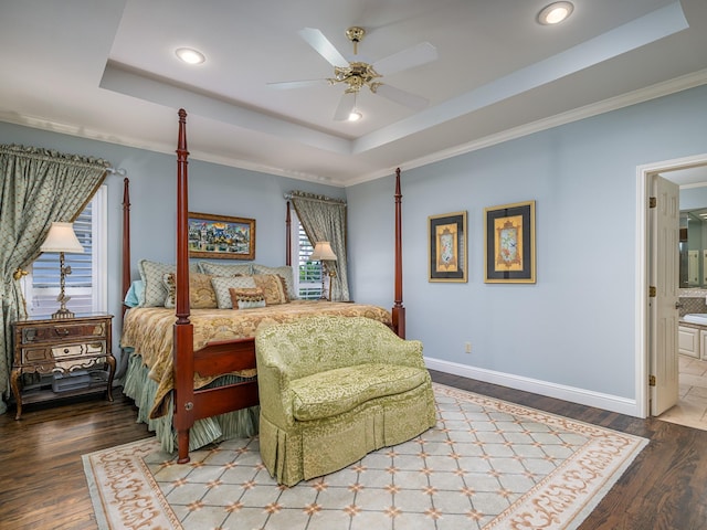 bedroom with wood-type flooring, ornamental molding, ensuite bath, and a tray ceiling