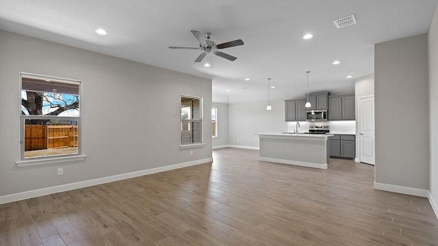 unfurnished living room with sink, ceiling fan, and light wood-type flooring