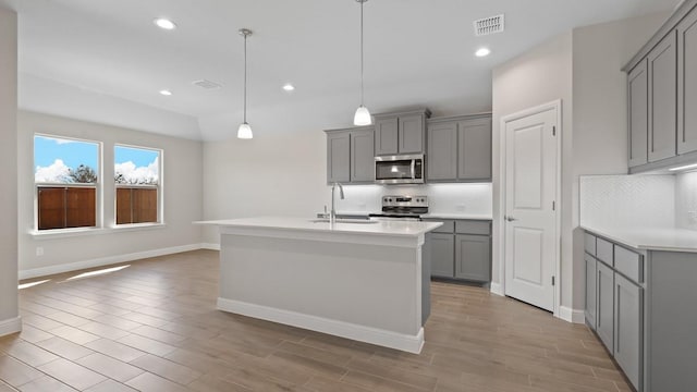 kitchen featuring sink, a center island with sink, gray cabinets, and appliances with stainless steel finishes