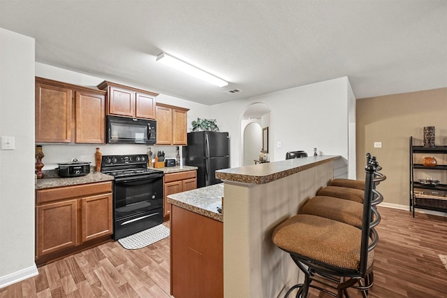 kitchen with a kitchen island, a breakfast bar area, light wood-type flooring, and black appliances