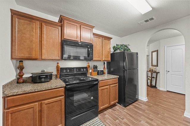 kitchen featuring light stone countertops, light hardwood / wood-style flooring, a textured ceiling, and black appliances